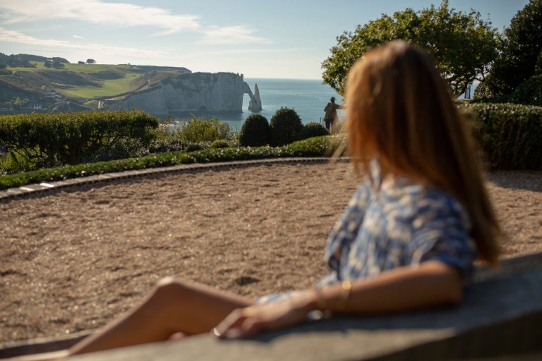 Une femme installée sur un banc profite du cadre et de la vue depuis les Jardins d'Etretat