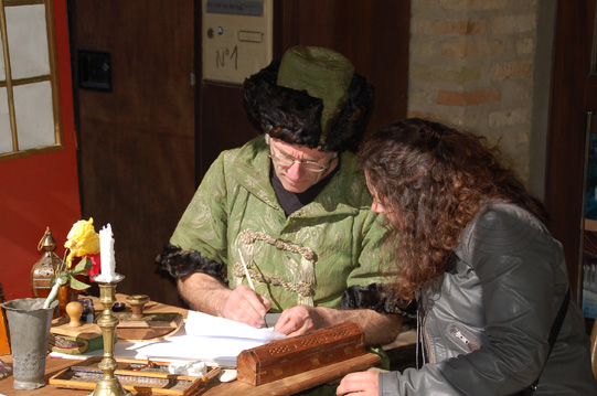 Artisan en costume médiéval, entrain d'écrire alors qu'une personne le regarde